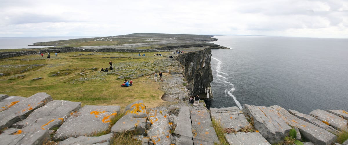 A coastal cliff with people sitting and walking on the grassy area.