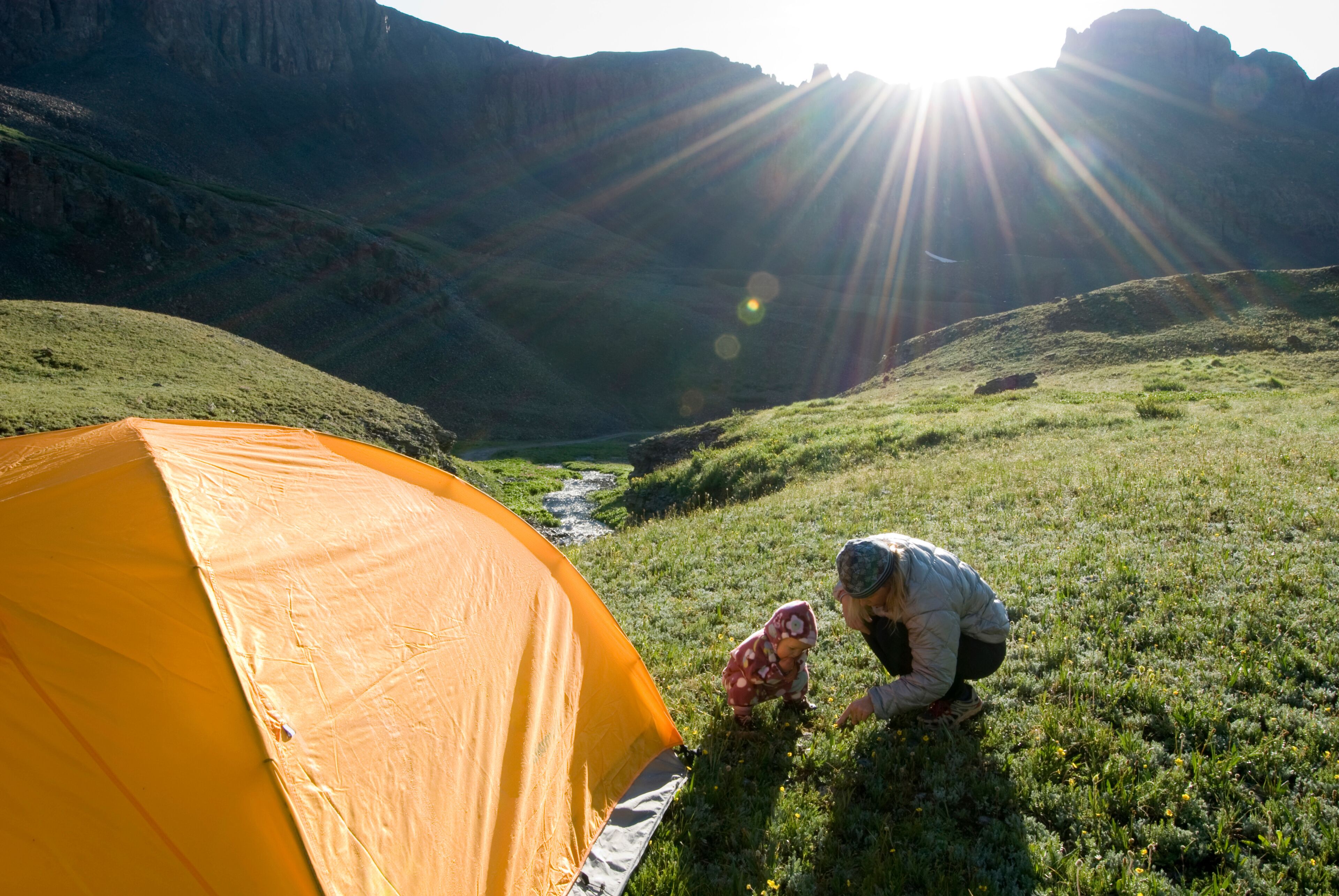 Una tienda de campaña montada en una ladera cubierta de hierba, con un río que serpentea por un cañón al fondo.
