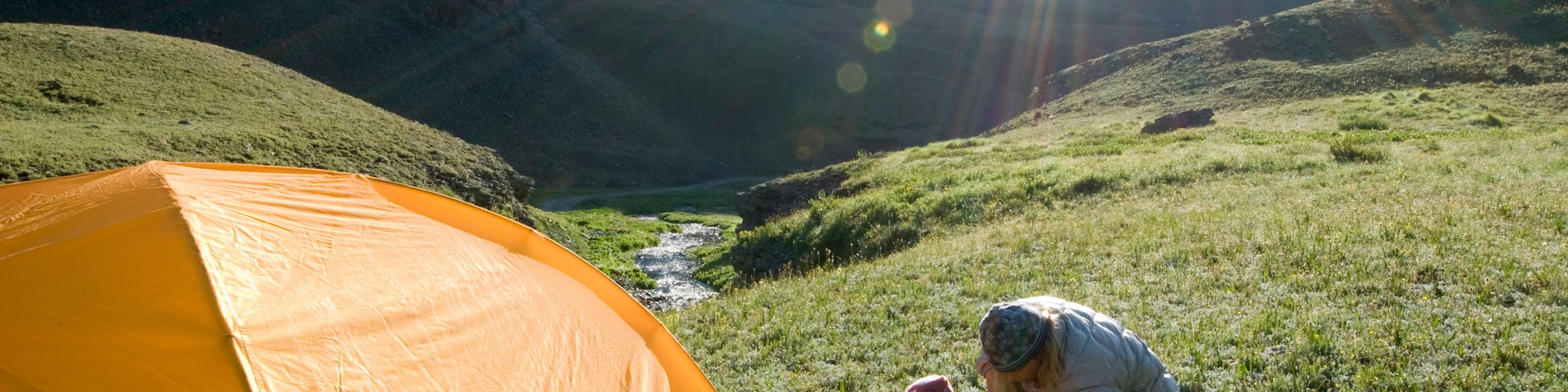 Una tienda de campaña montada en una ladera cubierta de hierba, con un río que serpentea por un cañón al fondo.