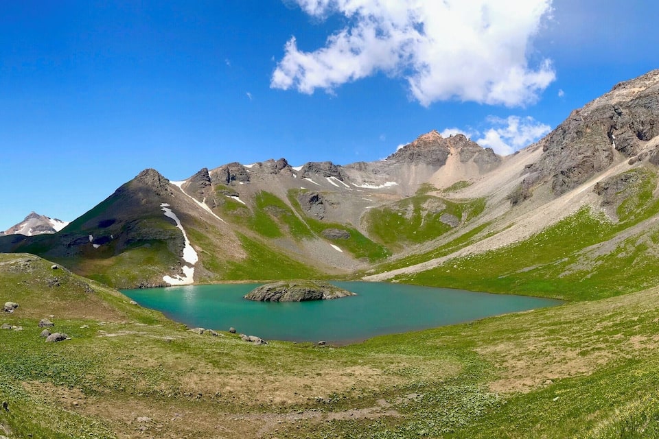 Een bergachtig landschap met een turquoise meer, omringd door groene heuvels en rotsachtige toppen.