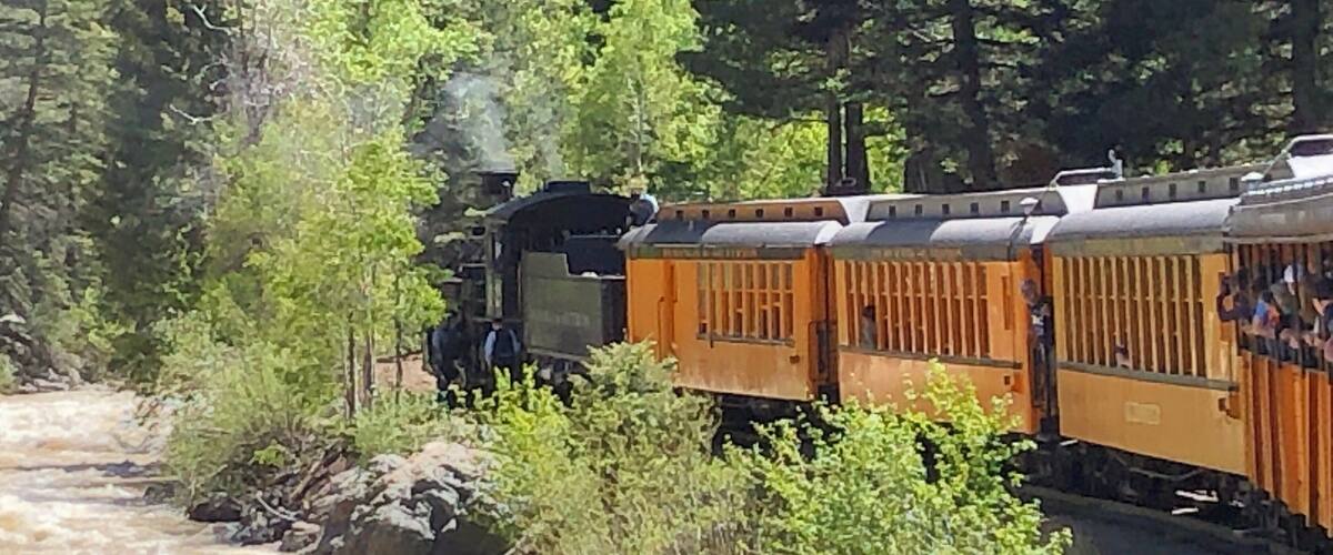 A train traveling through a forested area with a river on the left.