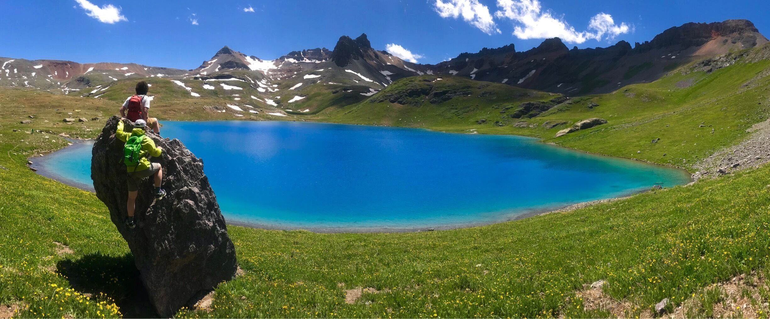 A person on a rock overlooking a turquoise lake surrounded by mountains.