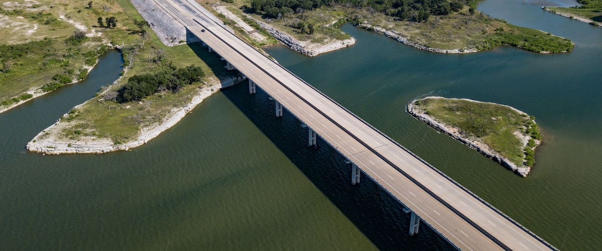 A bridge over a river with surrounding greenery and a distant water tower.