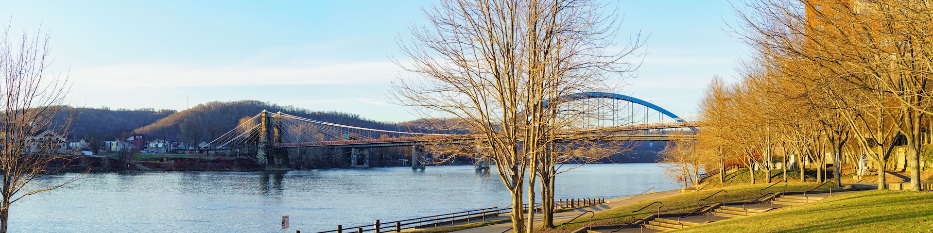 Panoramic view of the Ohio River with the landmark 1856 Wheeling Suspension Bridge and the 1955 Fort Henry Bridge, seen from Heritage Port waterfront park, Wheeling, West Virginia. January 2022.