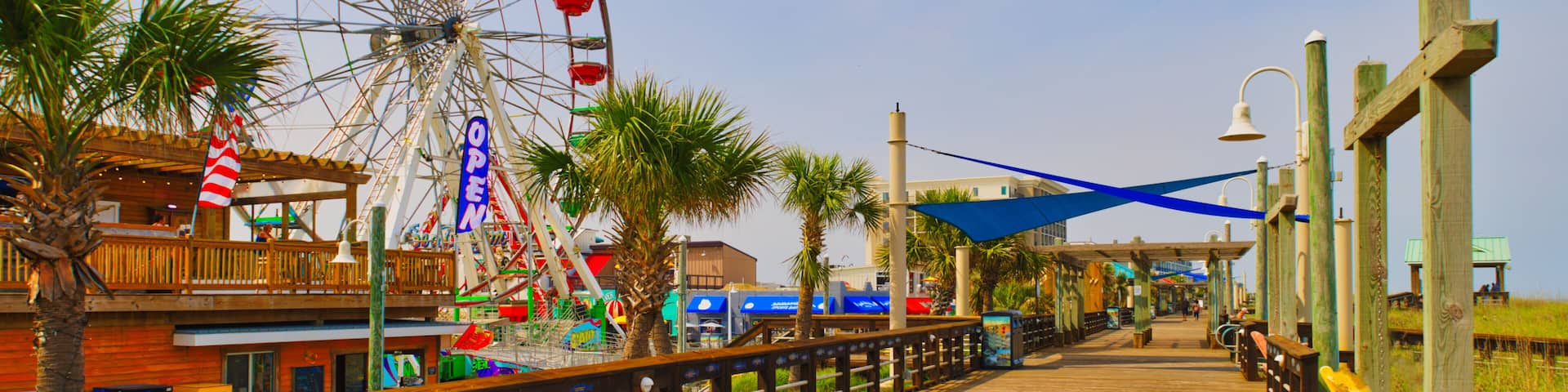 A sunny view down a wooden boardwalk and a large Ferris wheel at the Carolina Beach Amusement Park in Wilmington, North Carolina in the USA.