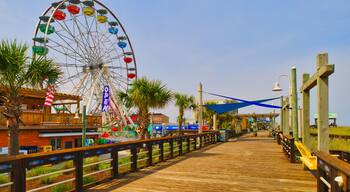 A sunny view down a wooden boardwalk and a large Ferris wheel at the Carolina Beach Amusement Park in Wilmington, North Carolina in the USA.