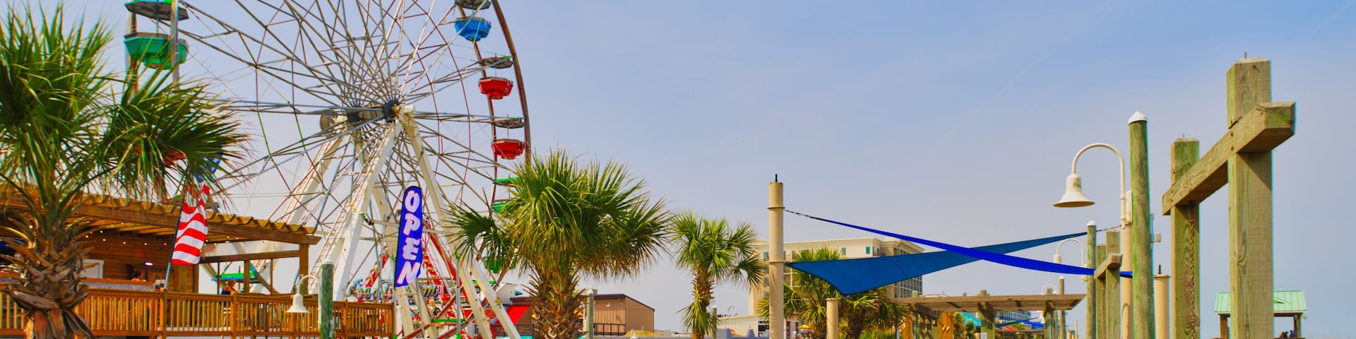 A sunny view down a wooden boardwalk and a large Ferris wheel at the Carolina Beach Amusement Park in Wilmington, North Carolina in the USA.