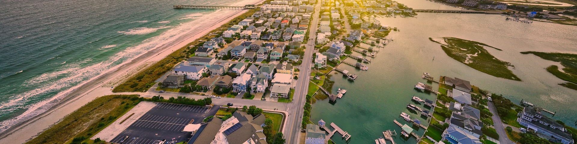 A coastal residential area with a beach, marina, and a pier extending into the water.