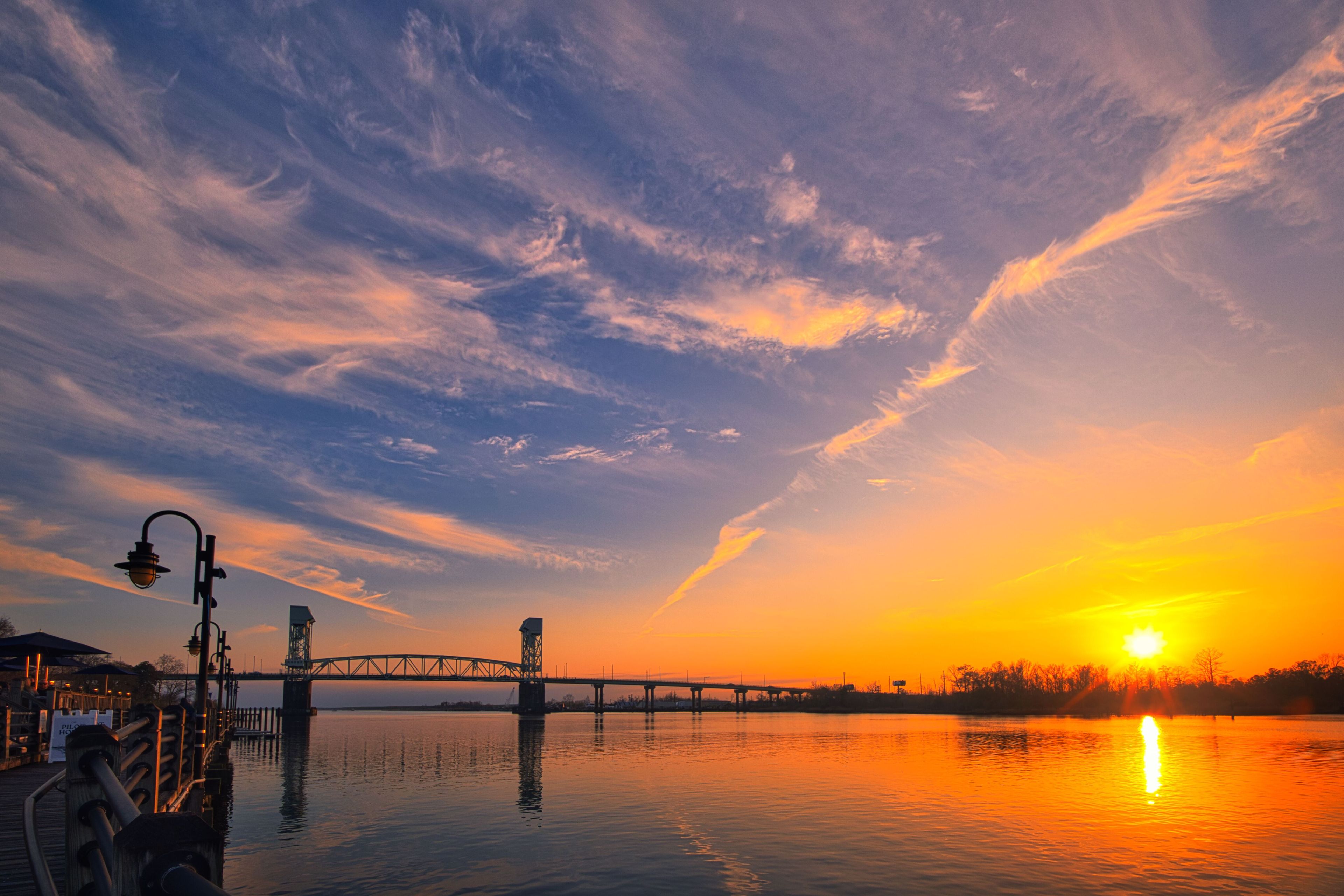 A sunset over a river with a bridge and street lamps.