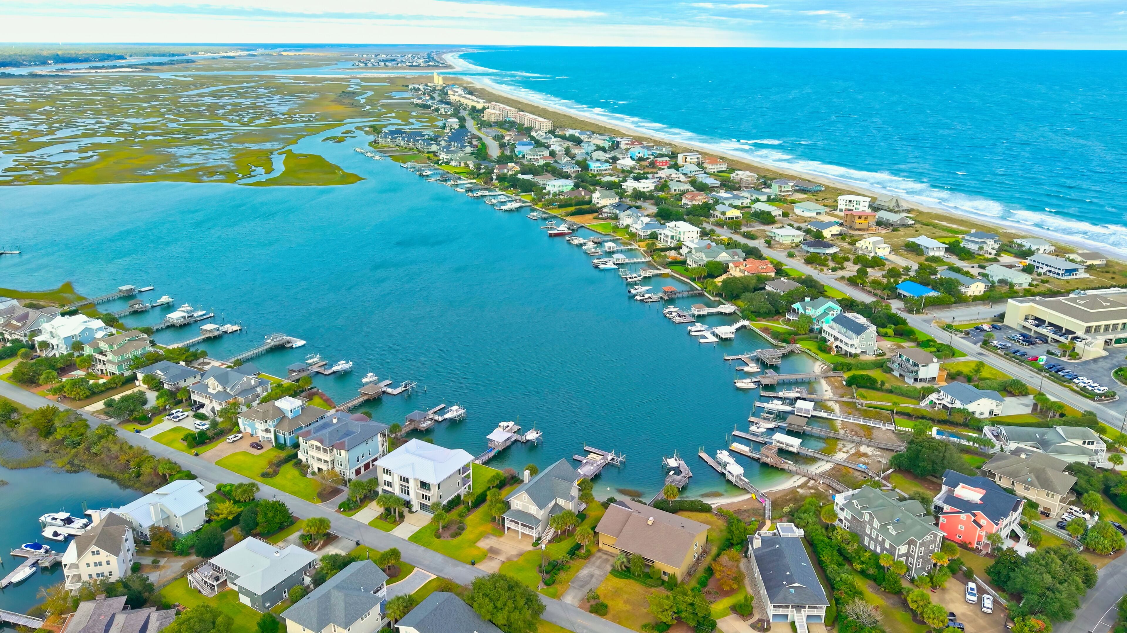 An aerial view of a coastal residential area with a marina, houses, and a beach.