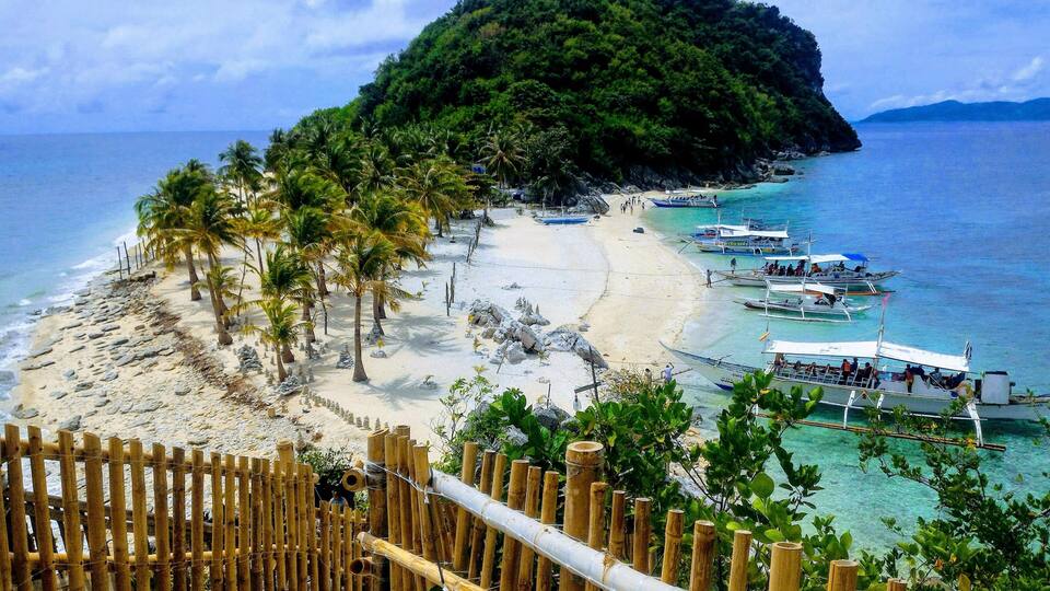 A beach with boats, palm trees, and a small island.