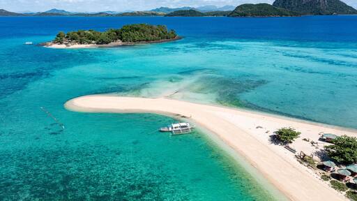 Aerial view of a pristine sandbar stretching into turquoise waters, connecting to a lush island paradise under a bright sky, Concepcion, Western Visayas, Philippines.