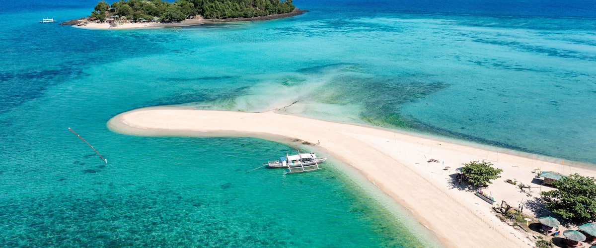 A tropical island with clear turquoise waters, a sandy beach, a boat, and lush greenery.