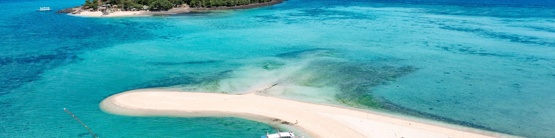 A tropical island with clear turquoise waters, a sandy beach, a boat, and lush greenery.