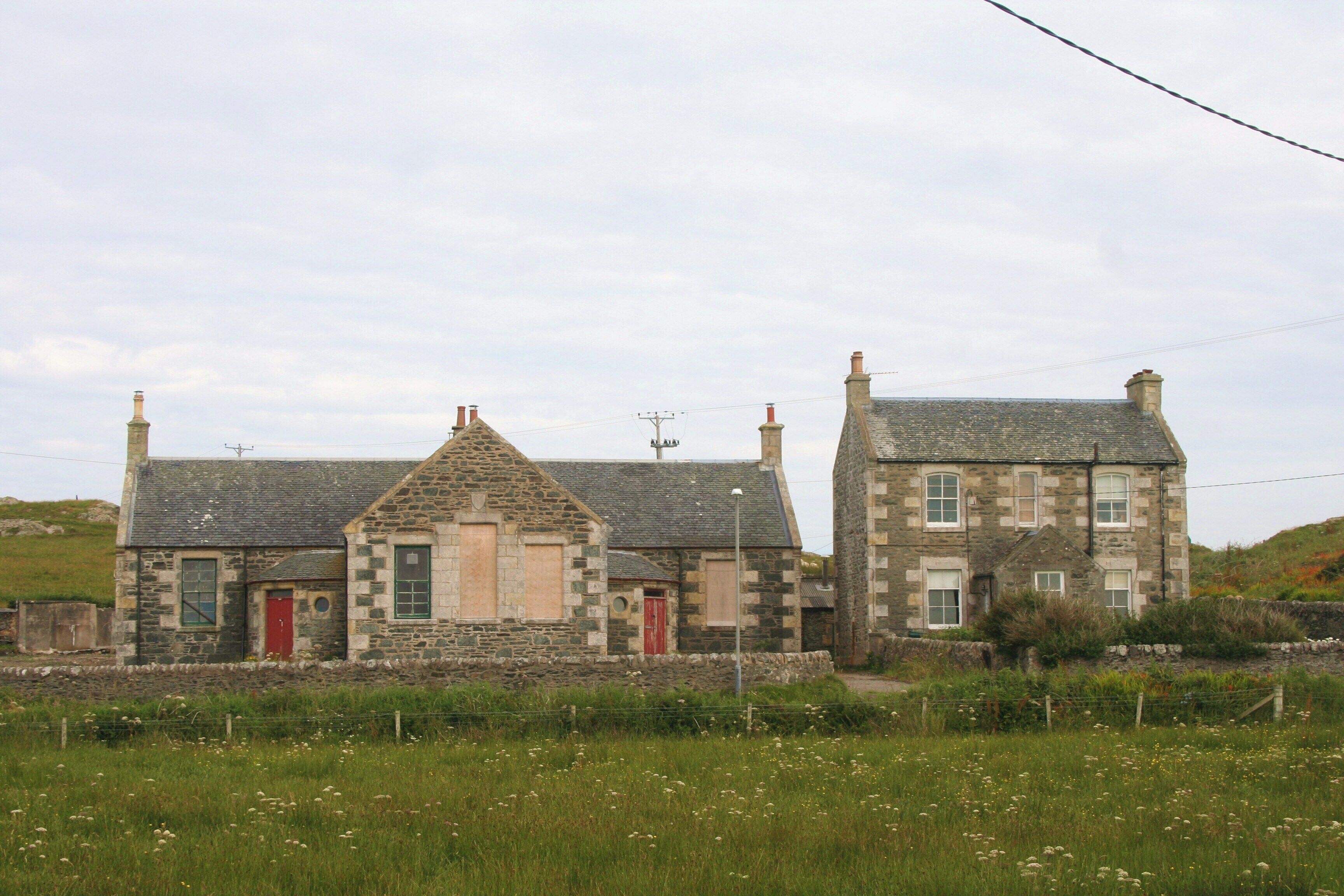 A stone house with a red door and chimney, surrounded by a grassy field.