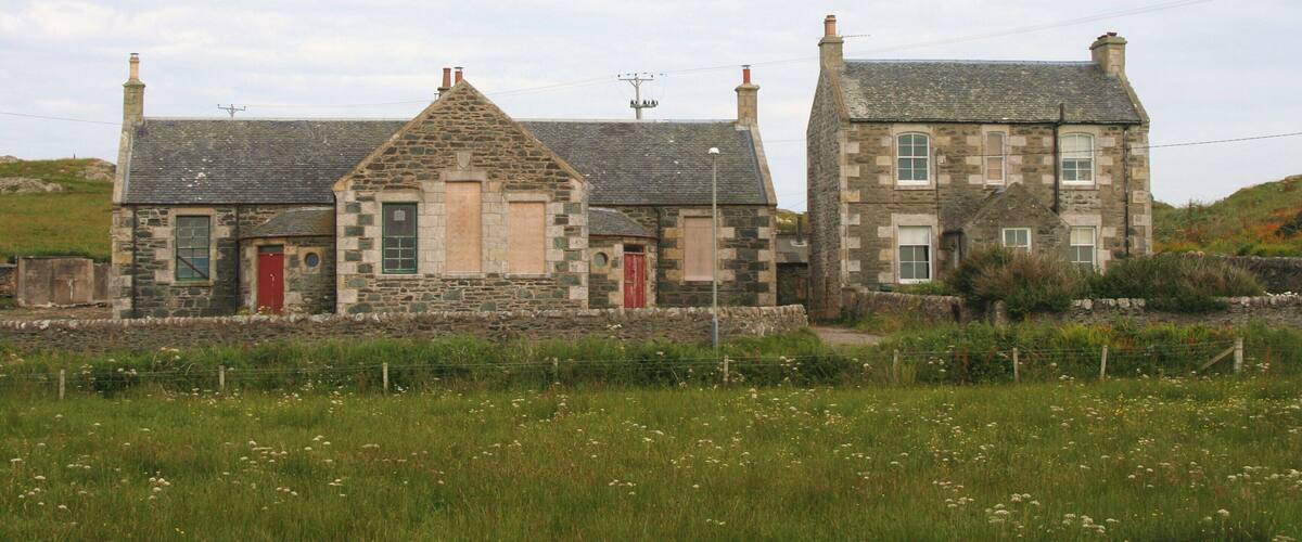 A stone house with a red door and chimney, surrounded by a grassy field.