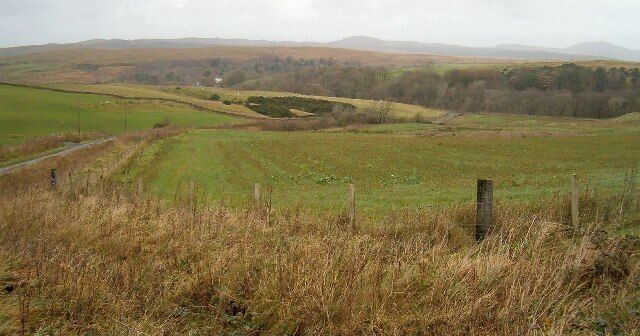A rural landscape with rolling hills, a road, and a fence.