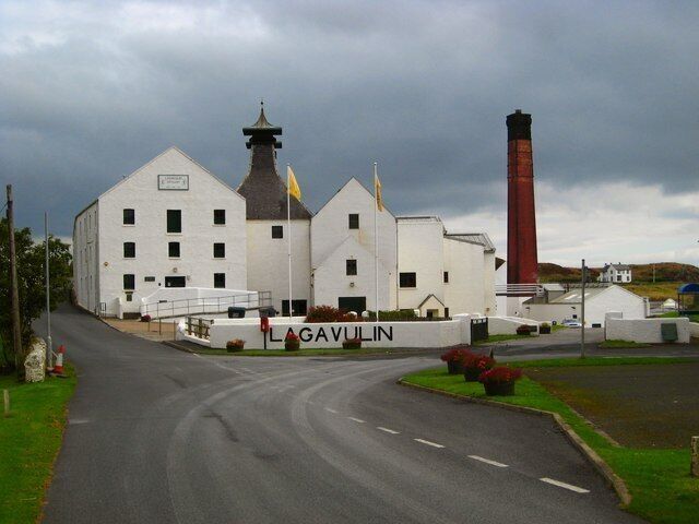 A white building with a red chimney, a sign reading "LAGAVULIN," and a road leading to it.
