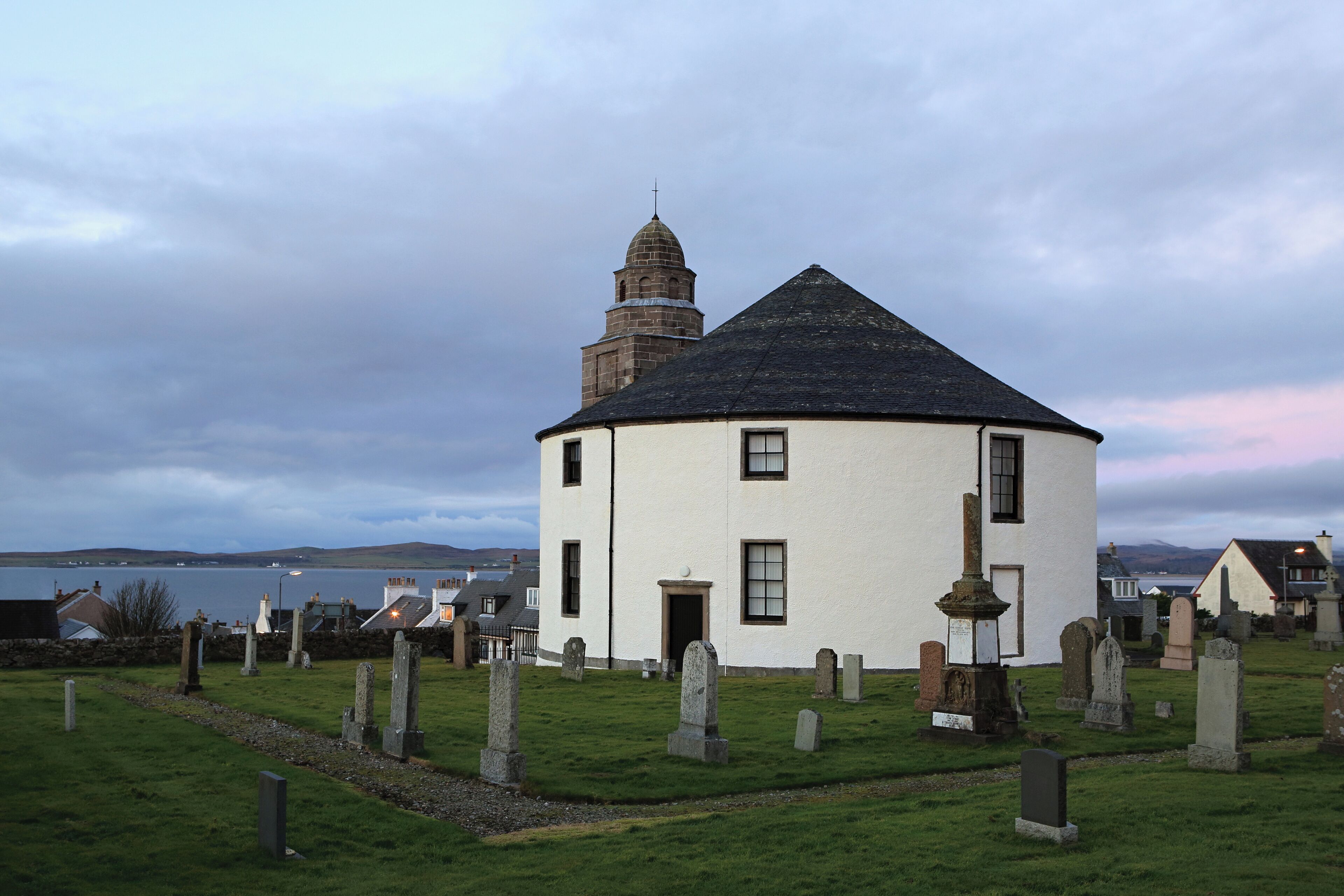 A white church with a bell tower and a graveyard with headstones.
