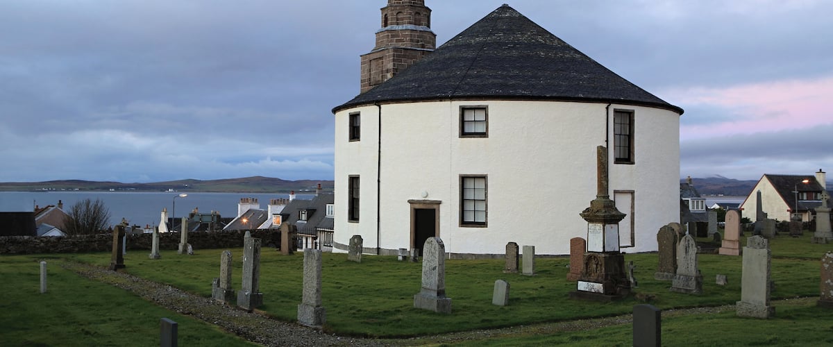 A white church with a bell tower and a graveyard with headstones.