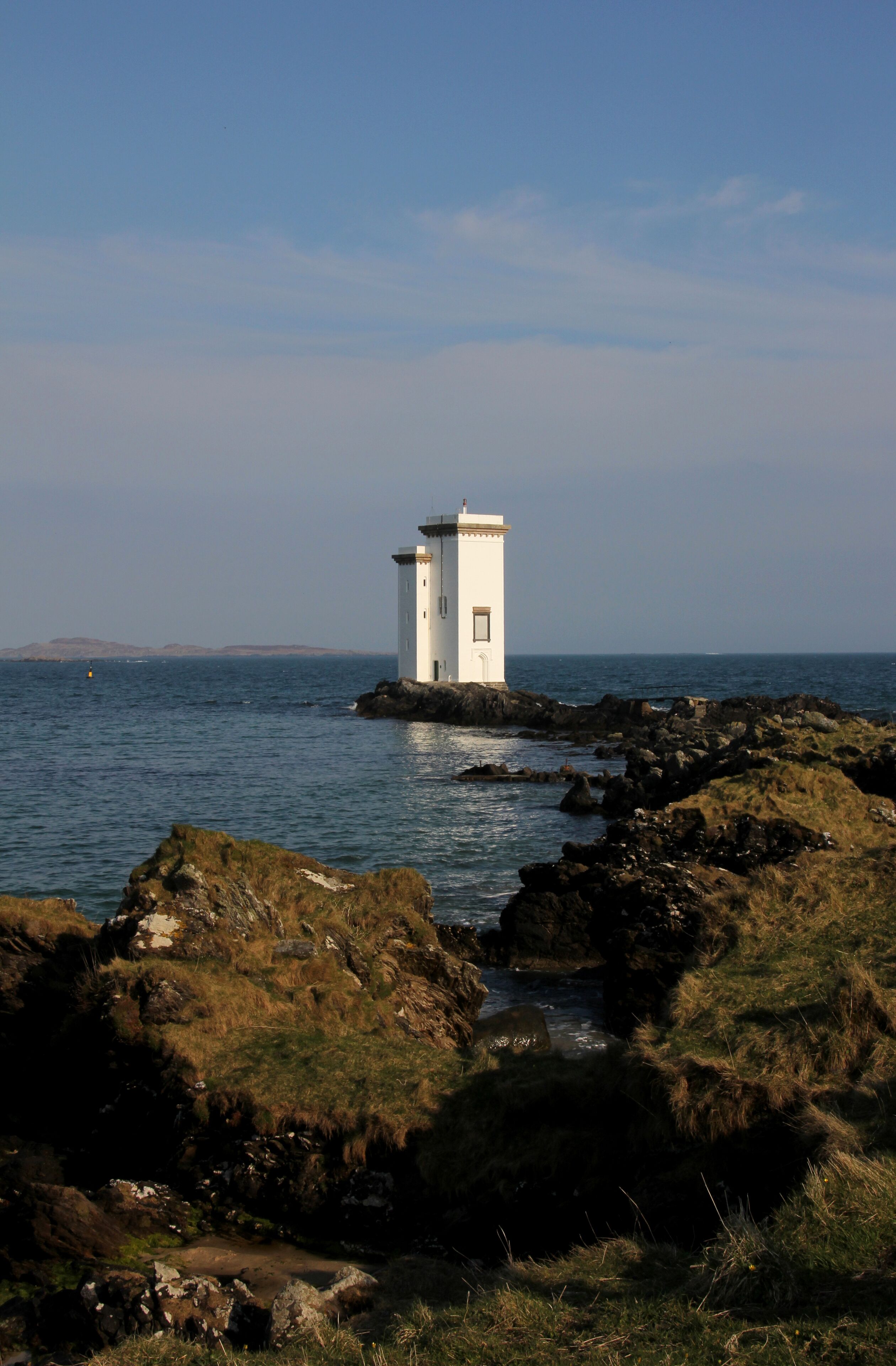 A lighthouse on a rocky coastline with calm waters.