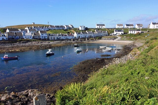 A coastal village with houses along the shore, boats in the water, and a clear sky.