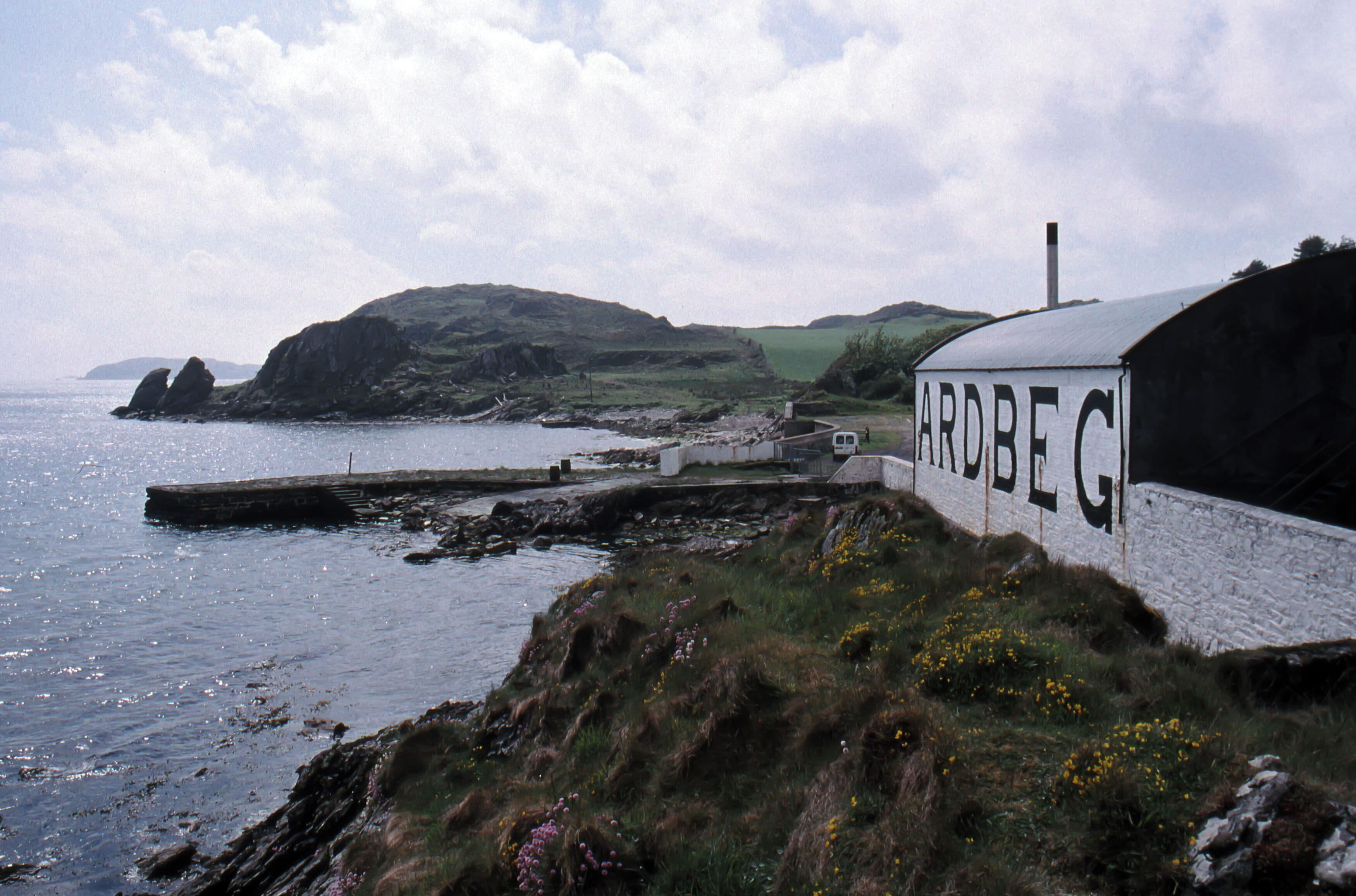 A coastal landscape with a white building labeled "ARDBEGI" and a rocky shoreline.