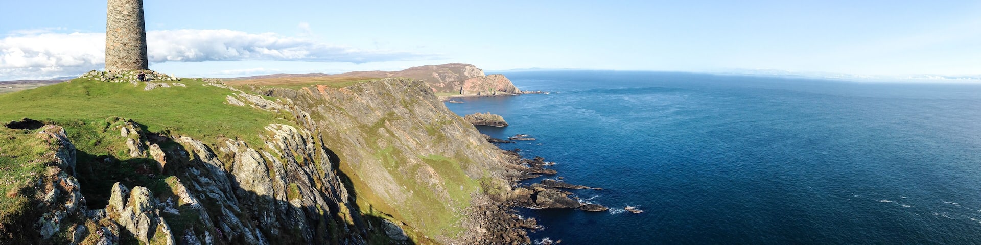 A large rock tower sits on a grassy field at the tip of the Oa Peninsula on the island of Islay in Scotland.