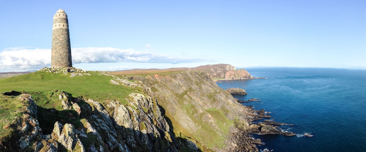 A stone tower on a grassy cliff overlooking a coastal sea.