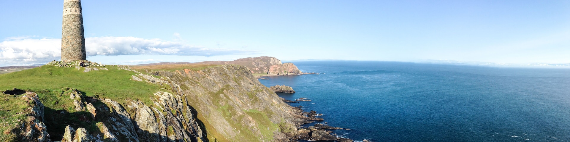 A stone tower on a grassy cliff overlooking a coastal sea.