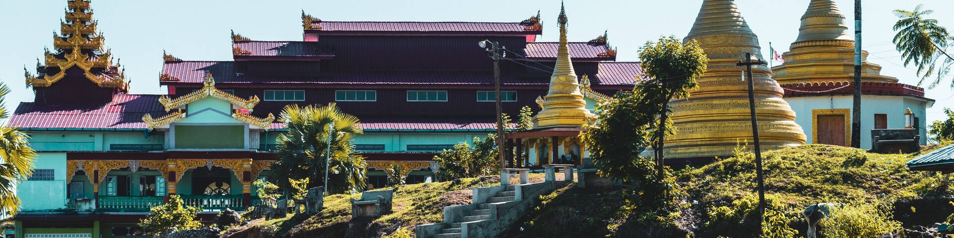 A traditional temple complex with ornate golden spires, a multi-tiered roof, and a lush green landscape.