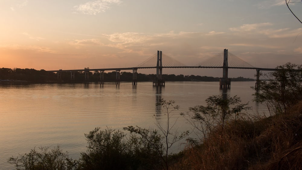 A suspension bridge over a calm river at sunset.