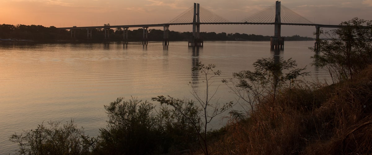 A suspension bridge over a calm river at sunset.