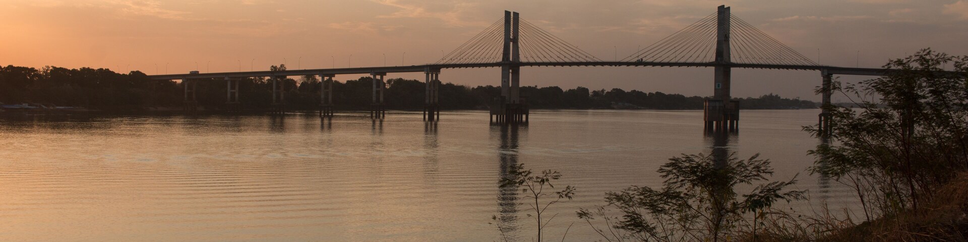A suspension bridge over a calm river at sunset.