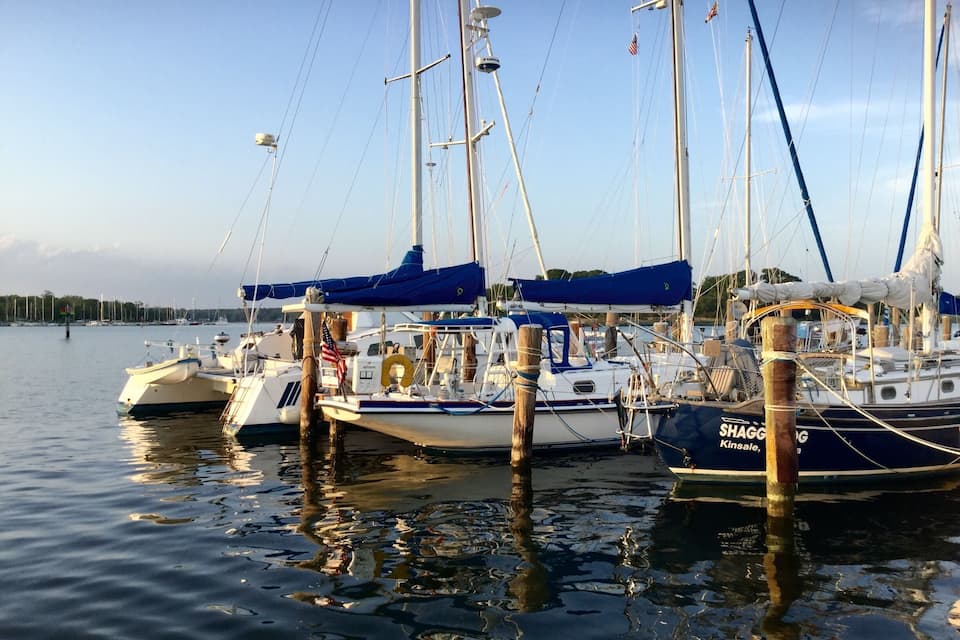A marina with several sailboats docked, featuring masts, sails, and American flags.