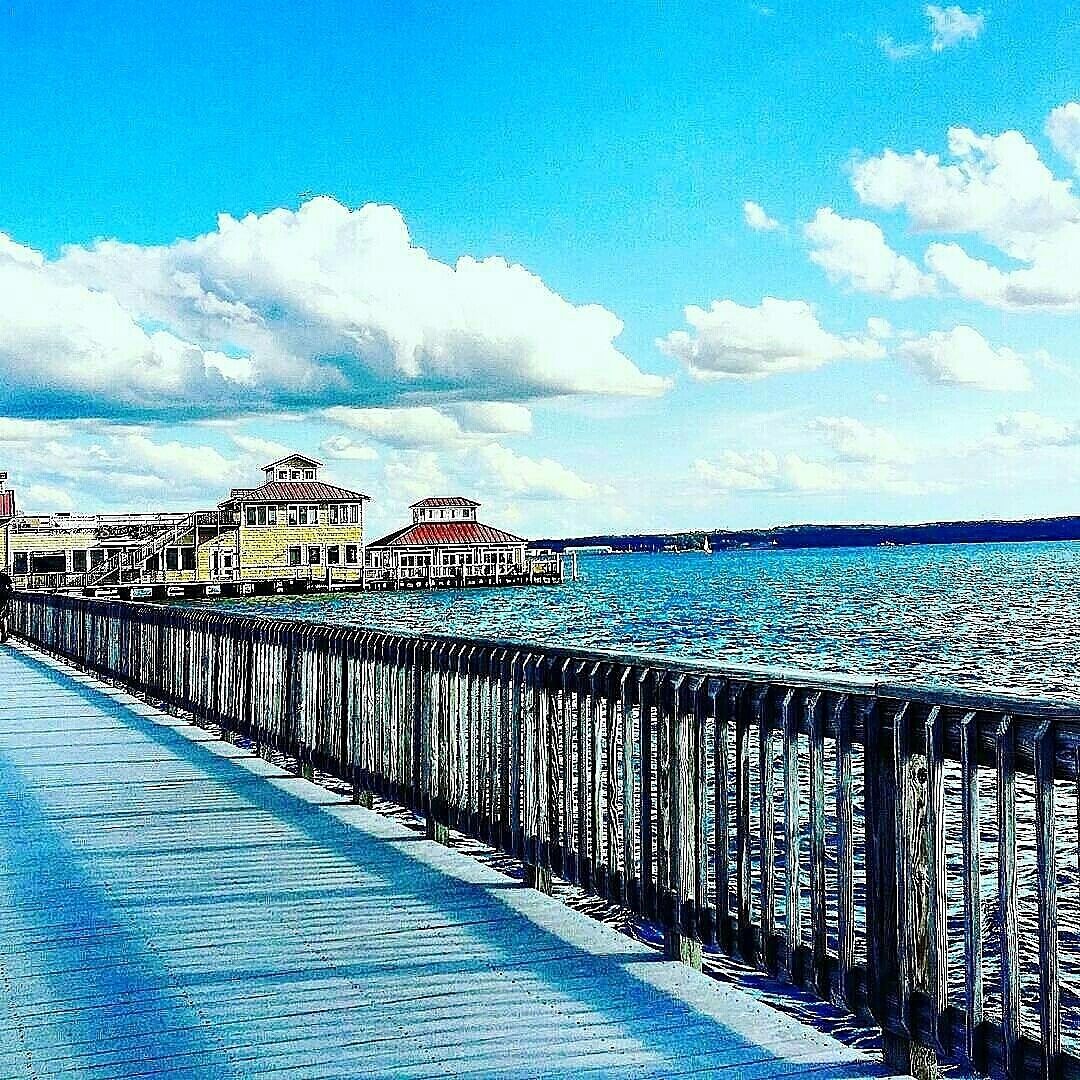 A waterfront promenade with a wooden walkway and buildings with red roofs.