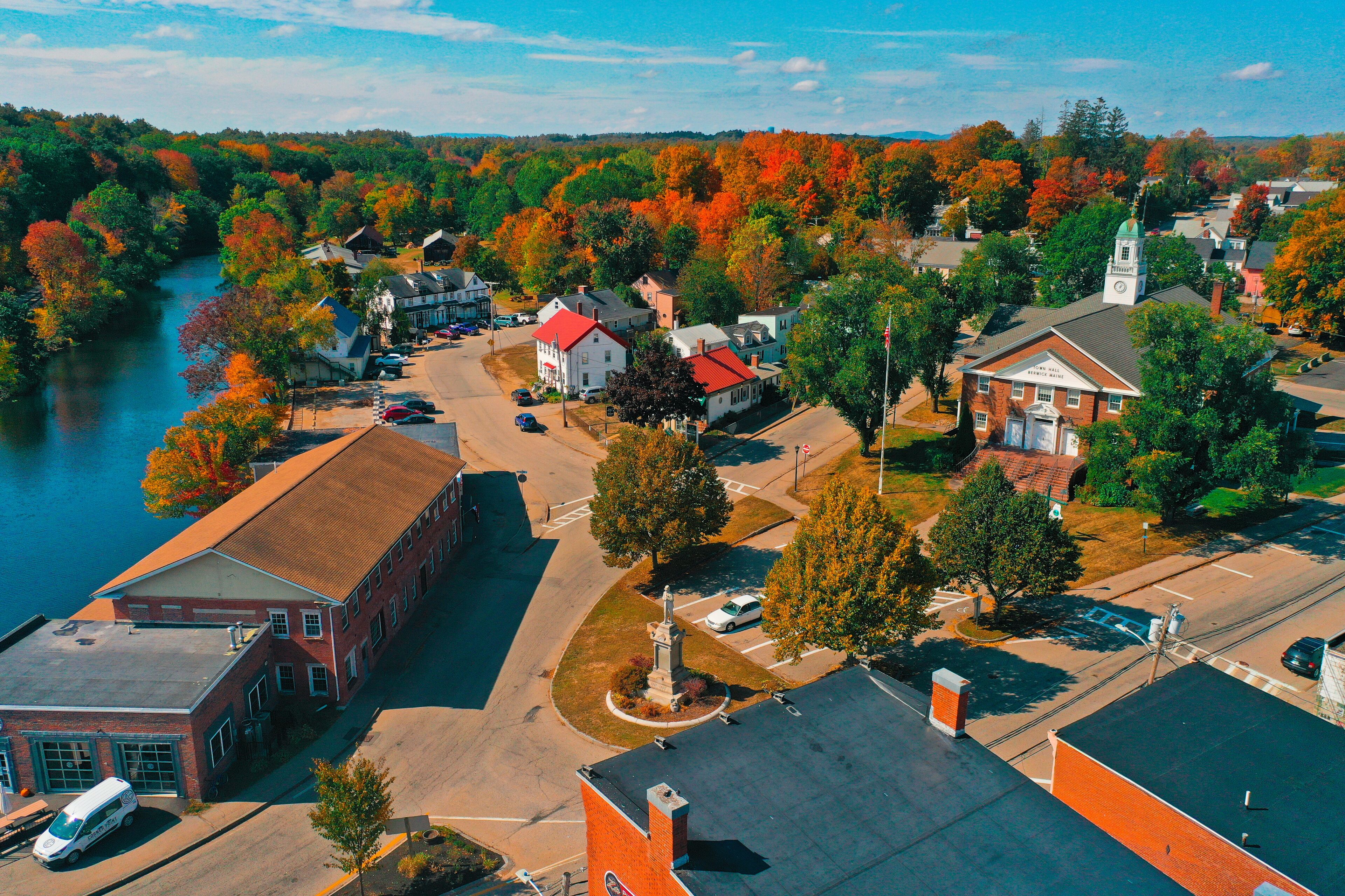 A riverside town with autumn foliage, a church steeple, and a prominent red brick building.