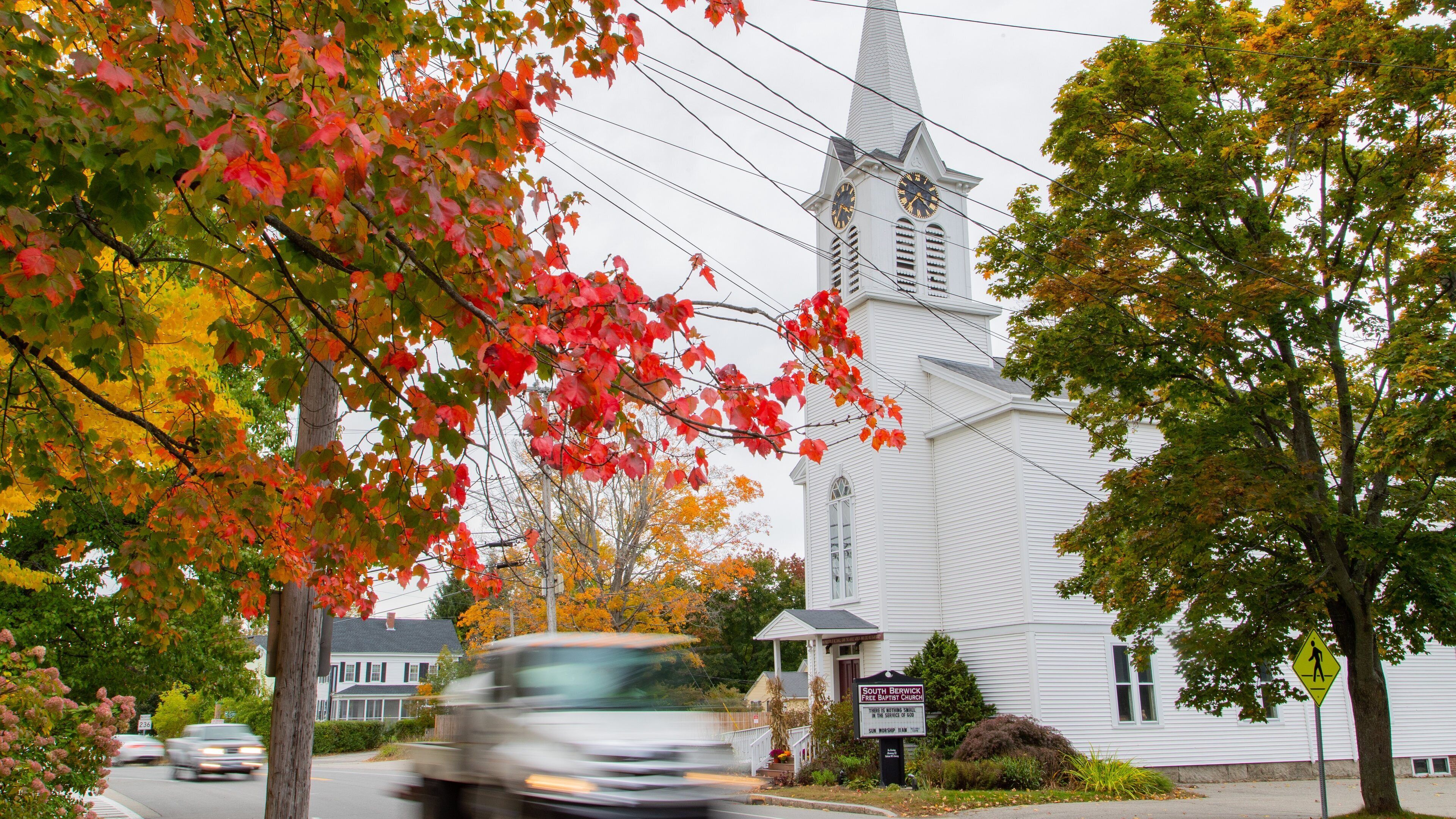A church with a steeple and a signboard in front.