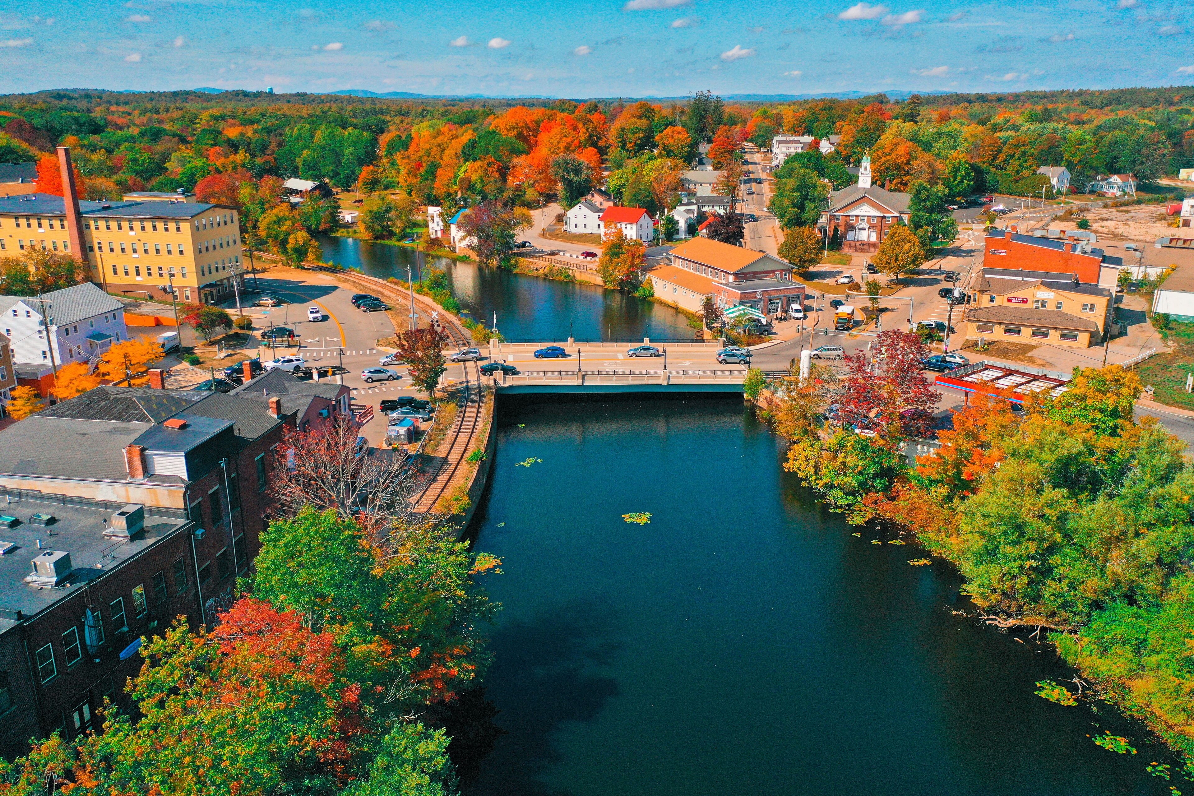 A river flowing through a town with autumn foliage, a bridge, and buildings.
