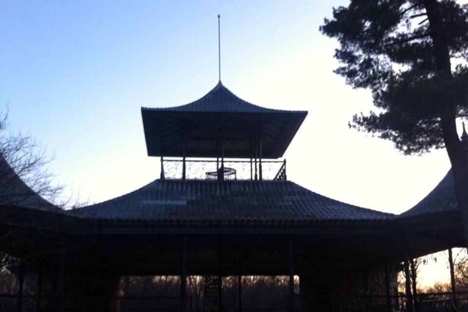 A traditional pavilion with a curved roof and a central tower, surrounded by trees and benches.