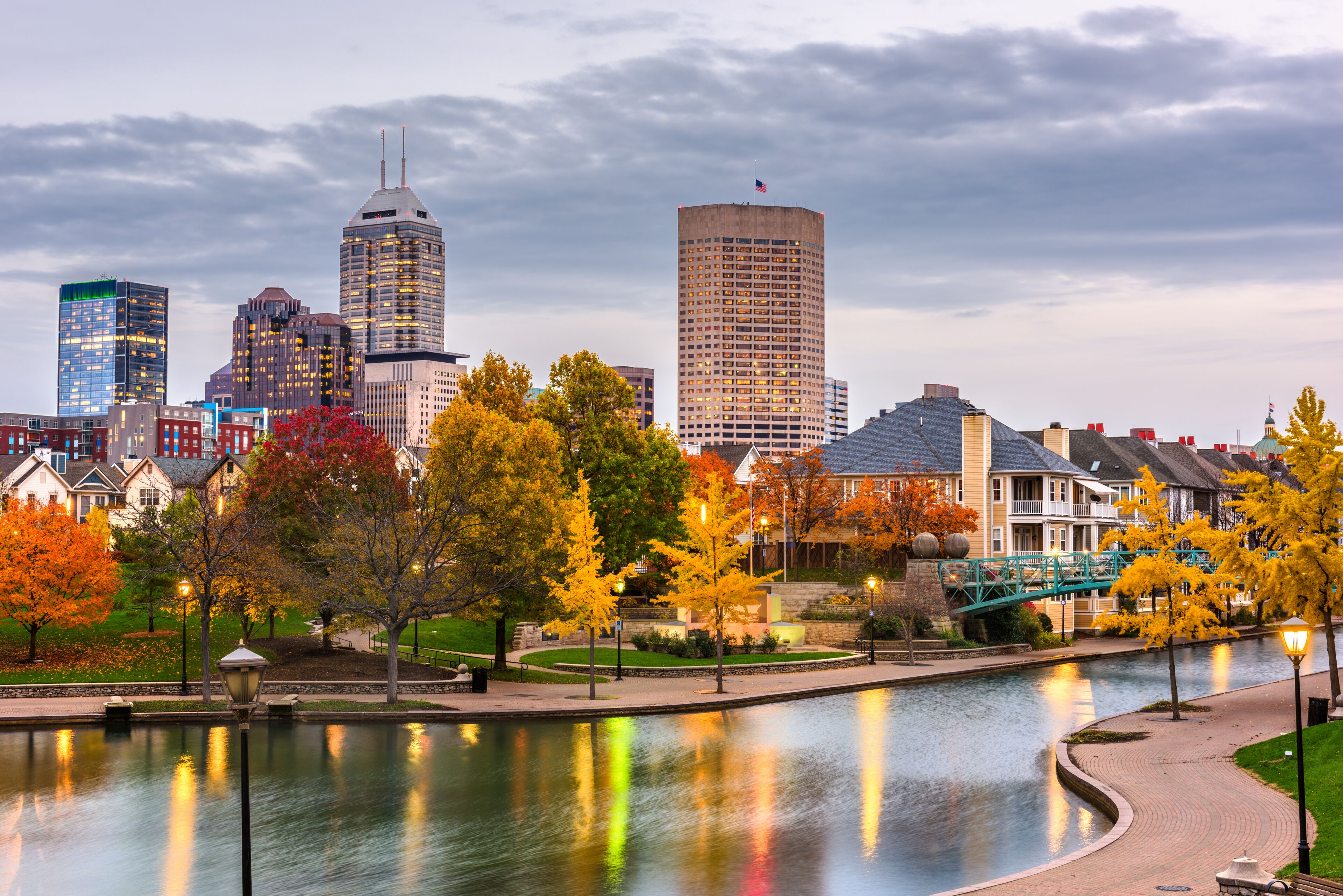 A city skyline with autumn-colored trees, a river reflecting lights, and a bridge.