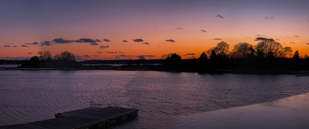 A sunset over a calm river with a dock and trees silhouetted against the sky.
