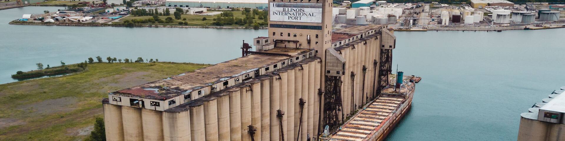 A large industrial complex with a prominent grain silo and a ship docked at a port.