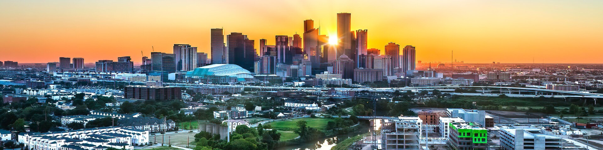 Un horizonte urbano al atardecer, con un río en primer plano y un estadio en el centro.