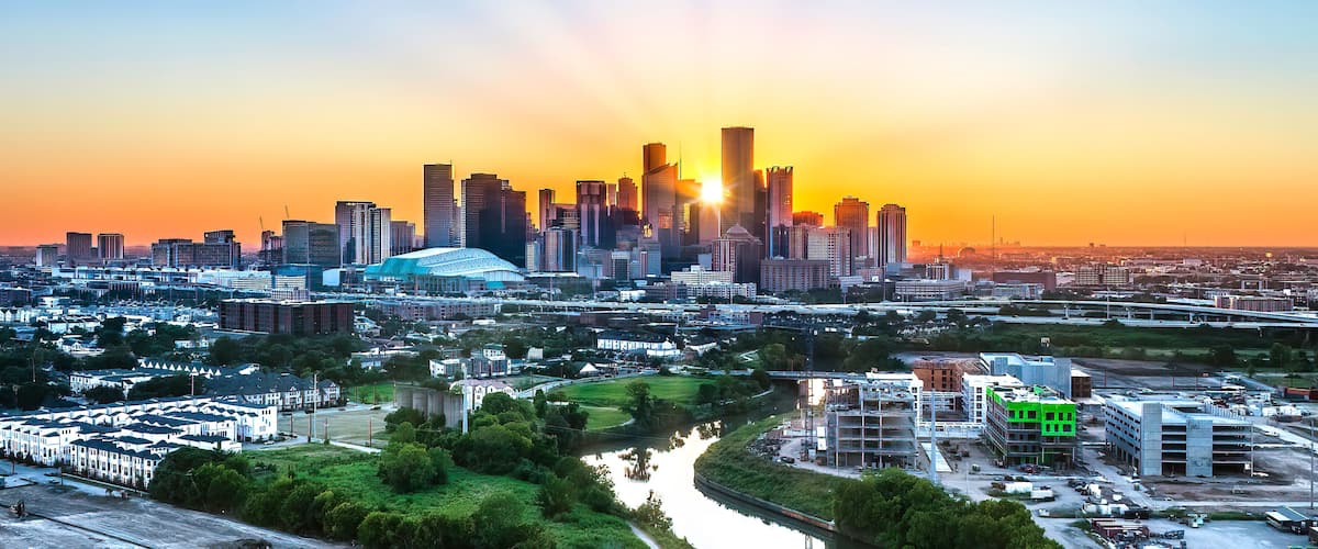 A city skyline at sunset with a river in the foreground and a stadium in the center.