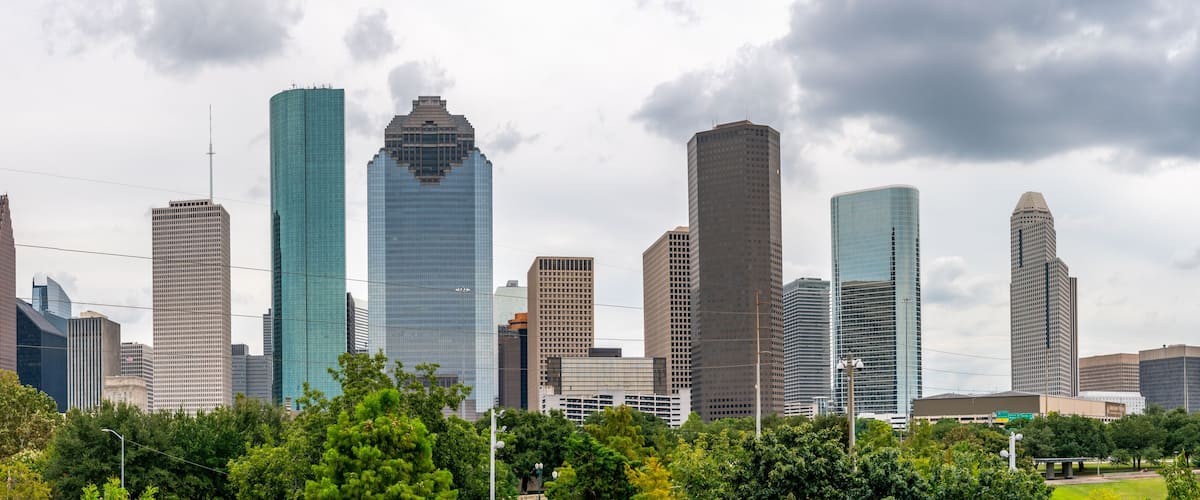 A city skyline with modern skyscrapers and lush green trees in the foreground.