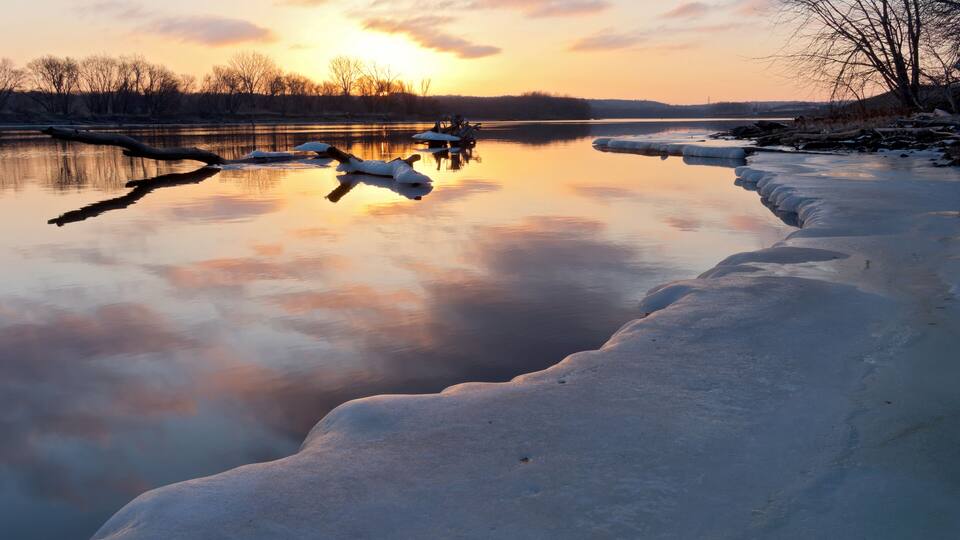 A frozen river with ice formations and a sunset in the background.