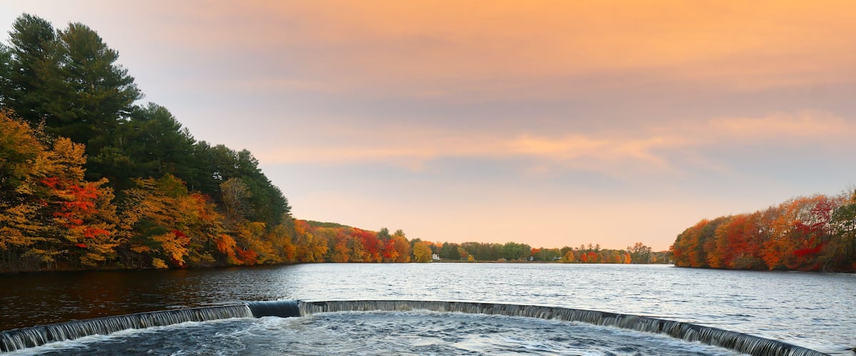 A river with a waterfall, surrounded by autumn-colored trees.