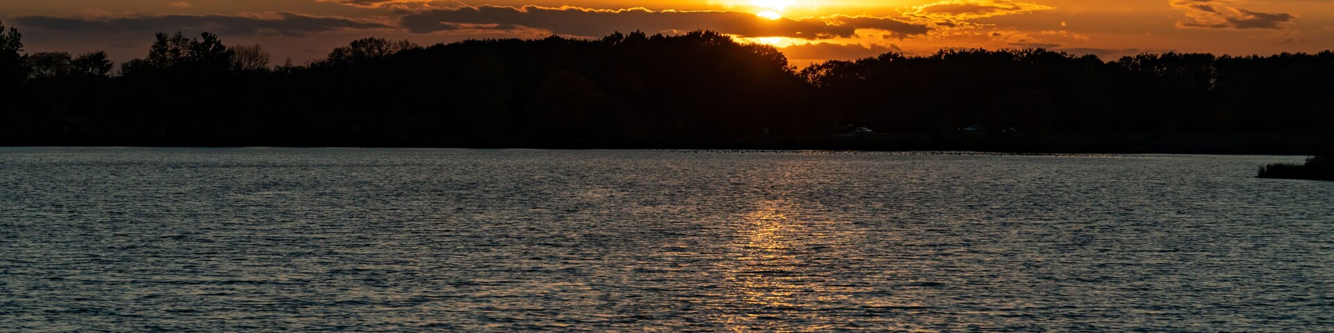 A sunset over a calm lake with trees silhouetted against the sky.