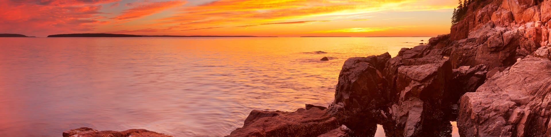 A coastal sunset with a lighthouse, rocky shoreline, and calm sea.